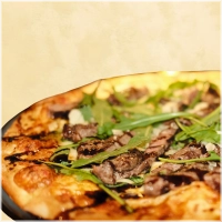 Pizza met dun gesneden ossenhaas, mozzarella, pesto, rucola, balsamico creme en Parmezaanse kaas